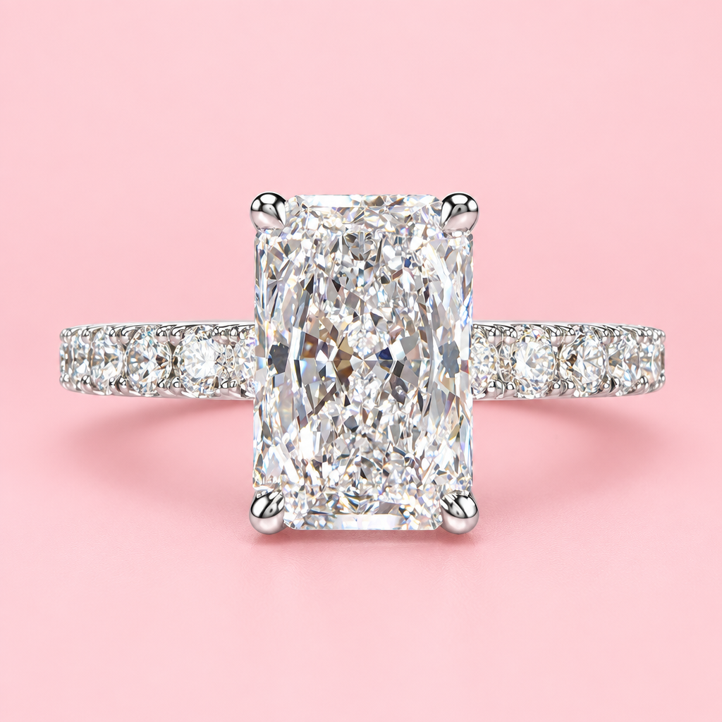A radiant-cut diamond engagement ring with a diamond pavé band, set in a silver-colored metal, centered on a solid pink background.