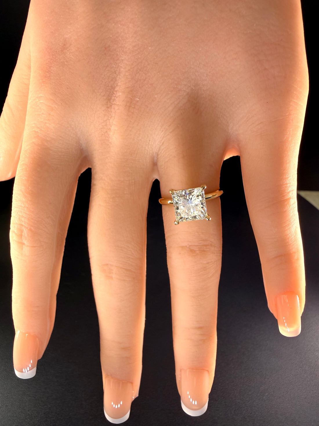 Princess-cut diamond ring with a plain yellow-gold band worn on a hand.