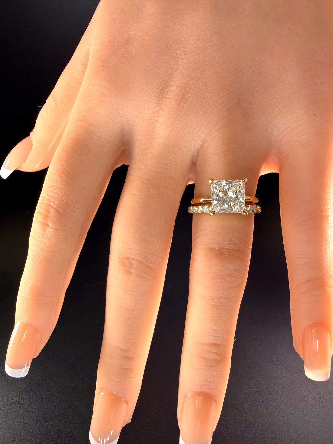 Princess-cut diamond solitaire with a plain yellow-gold band worn beside one separate diamond wedding band.