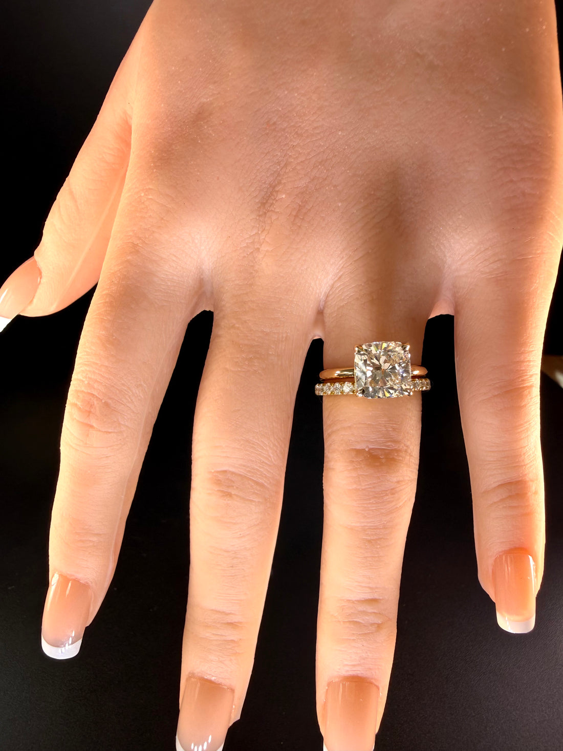 Cushion-cut diamond solitaire with a plain yellow-gold band worn beside one separate diamond wedding band.