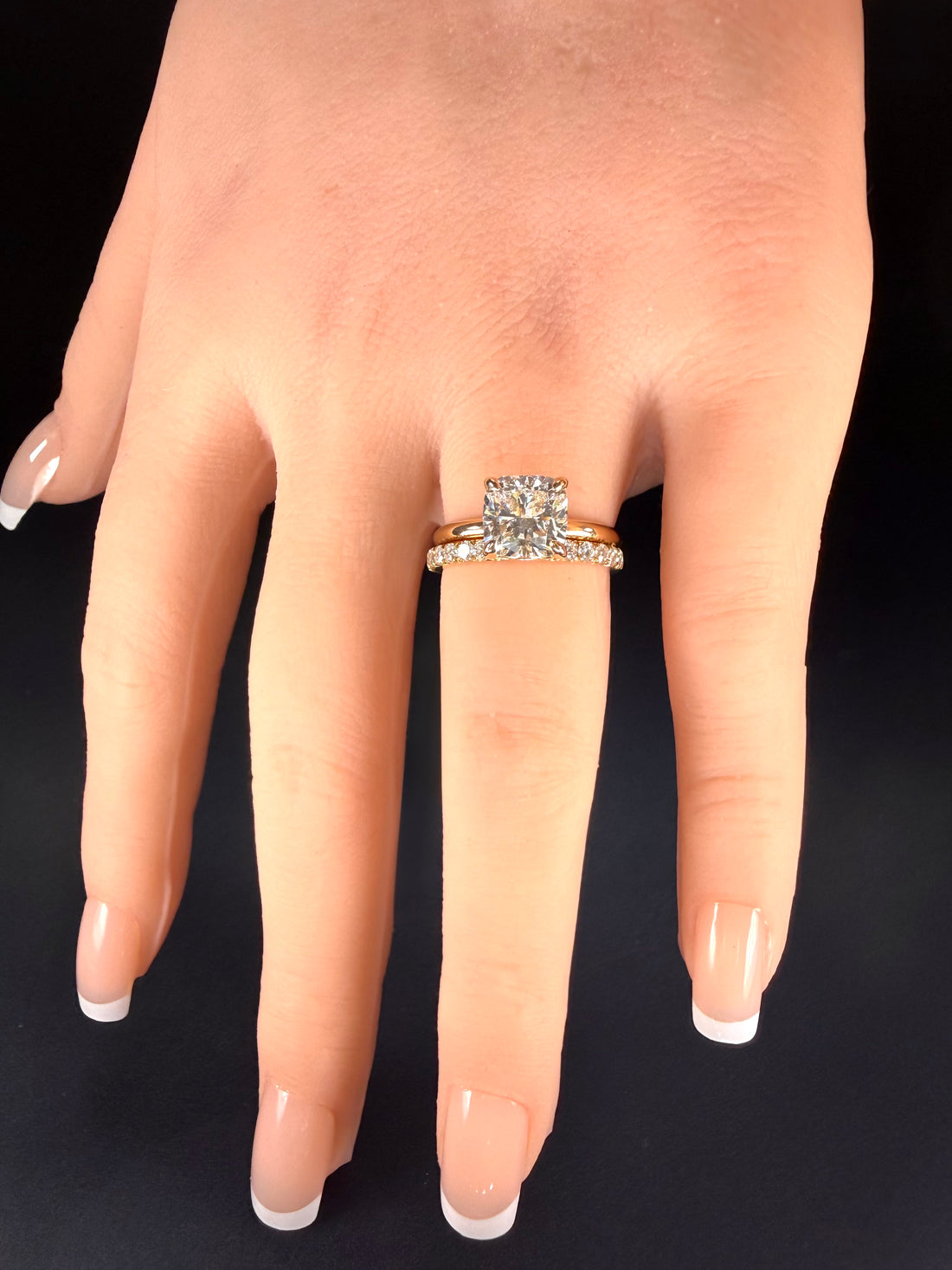 Cushion-cut diamond solitaire in yellow gold worn with one diamond-set band on a hand.