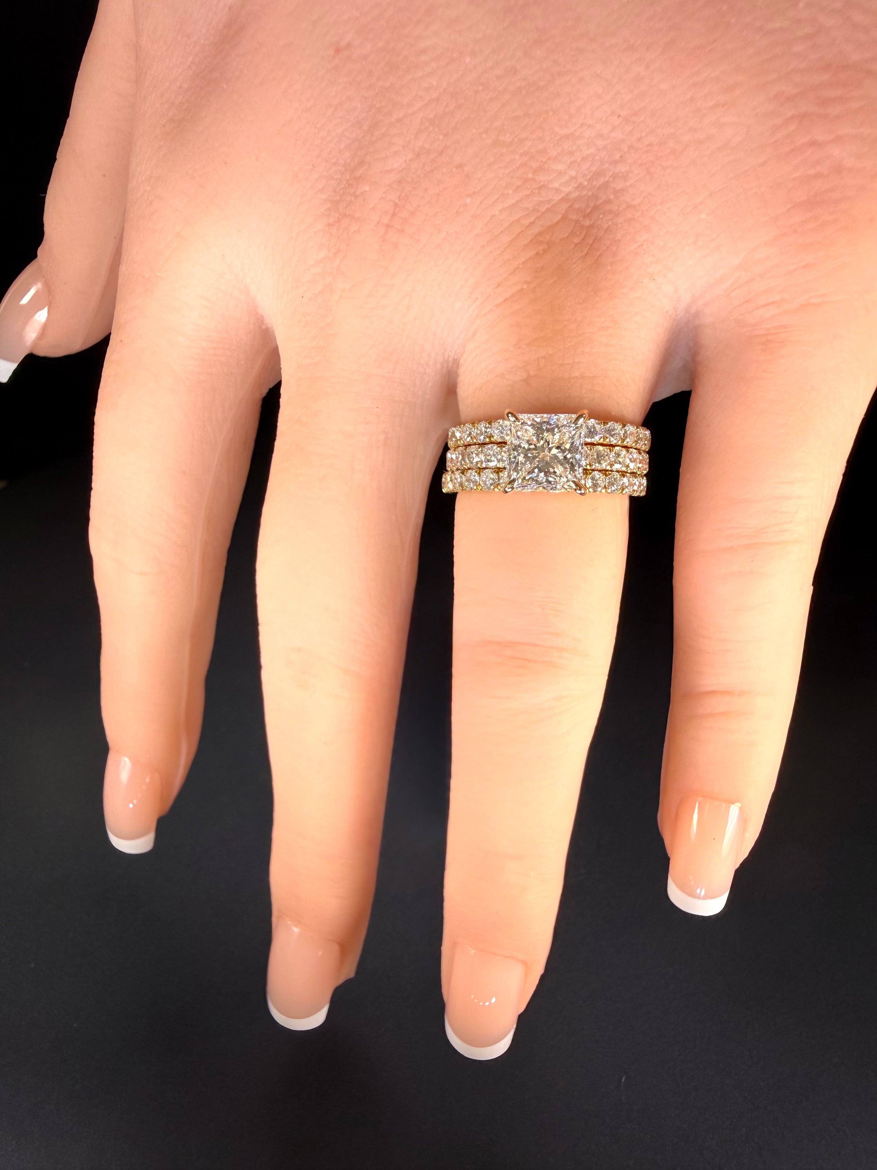 Princess-cut diamond pavé ring in yellow gold worn between two diamond-set bands on a hand.