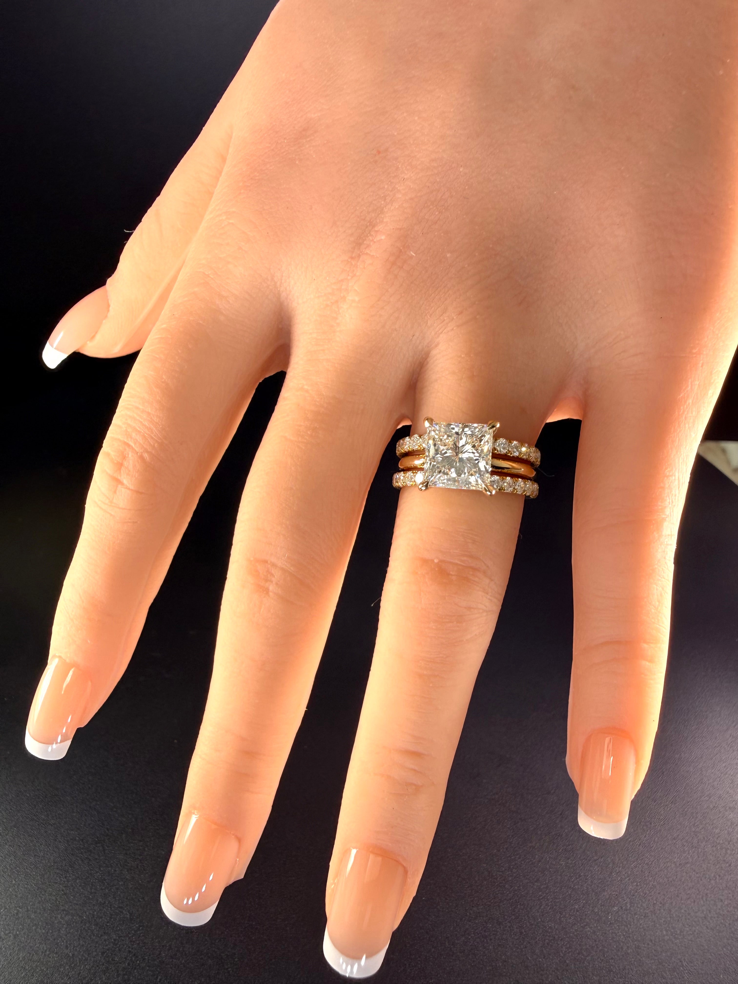 Princess-cut diamond solitaire worn between two separate diamond wedding bands on a hand against black.