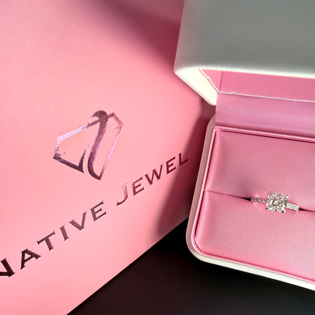Diamond ring in an open pink-lined presentation box beside a pink Native Jewel shopping bag.