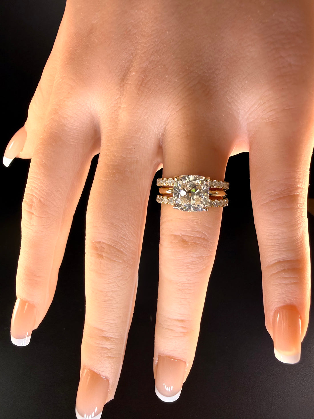 Cushion-cut diamond solitaire worn between two separate diamond wedding bands on a hand against black.