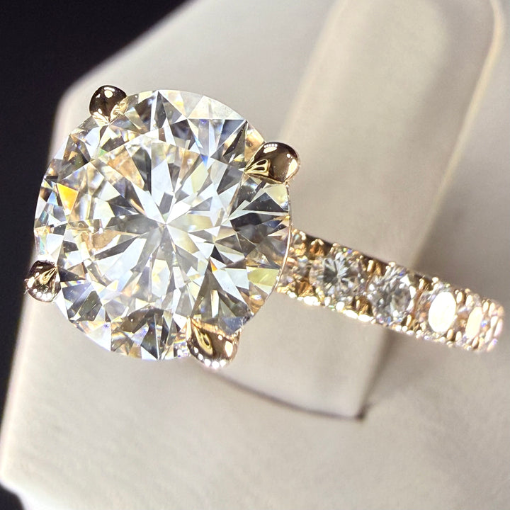 Angled close-up of a round diamond engagement ring showing yellow-gold prongs and the diamond-set shoulder.