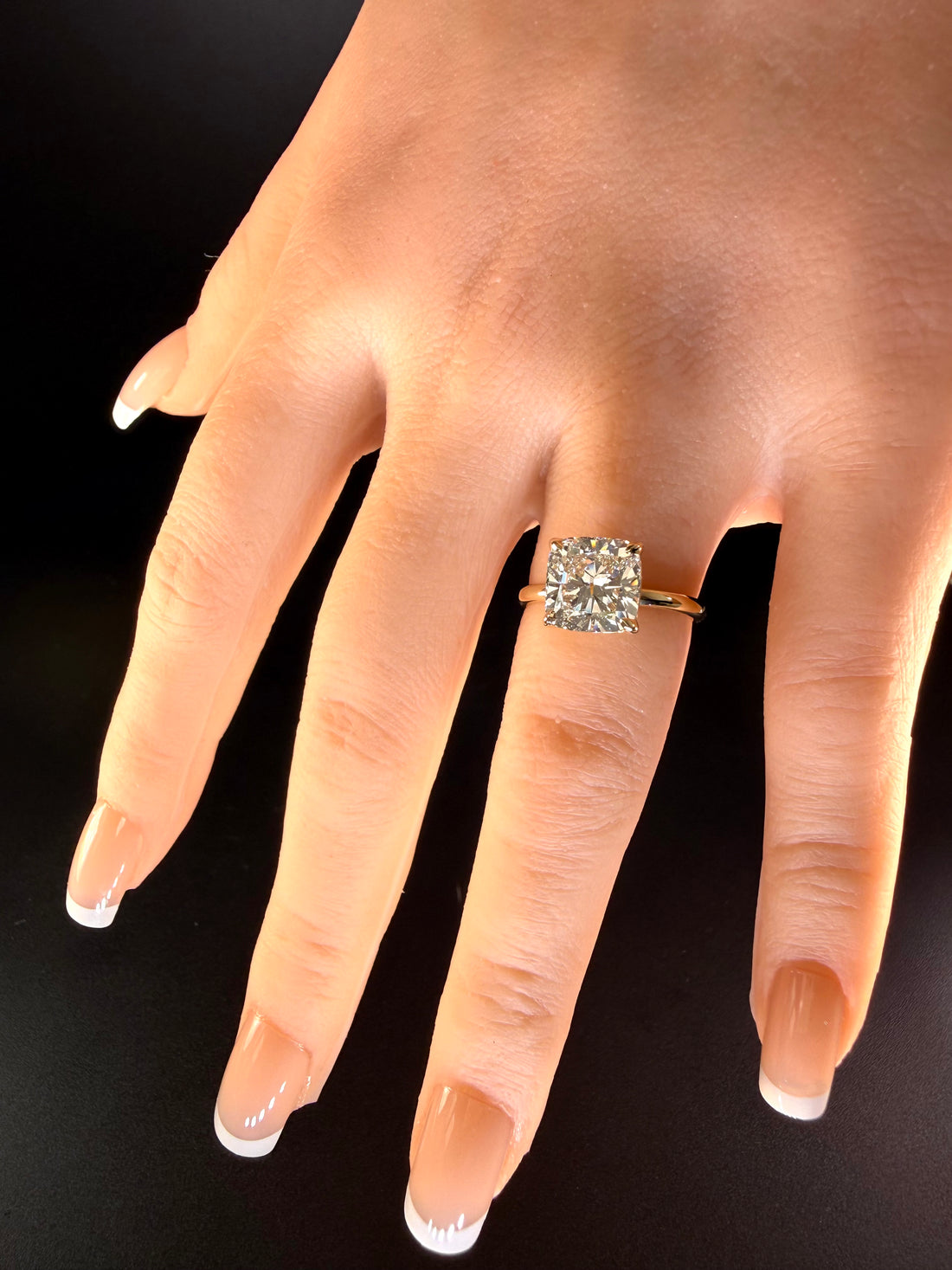 Diamond solitaire with four prongs and a polished yellow-gold band worn on a hand against a dark background.