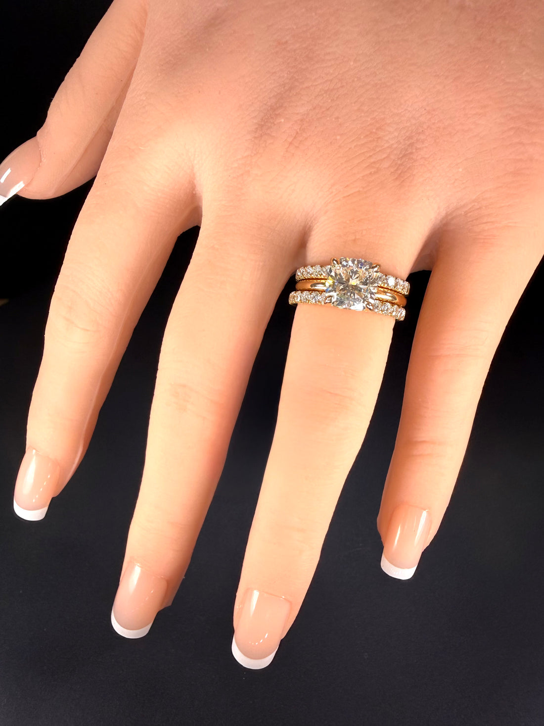 Cushion-cut diamond solitaire in yellow gold worn between two diamond-set bands on a hand.