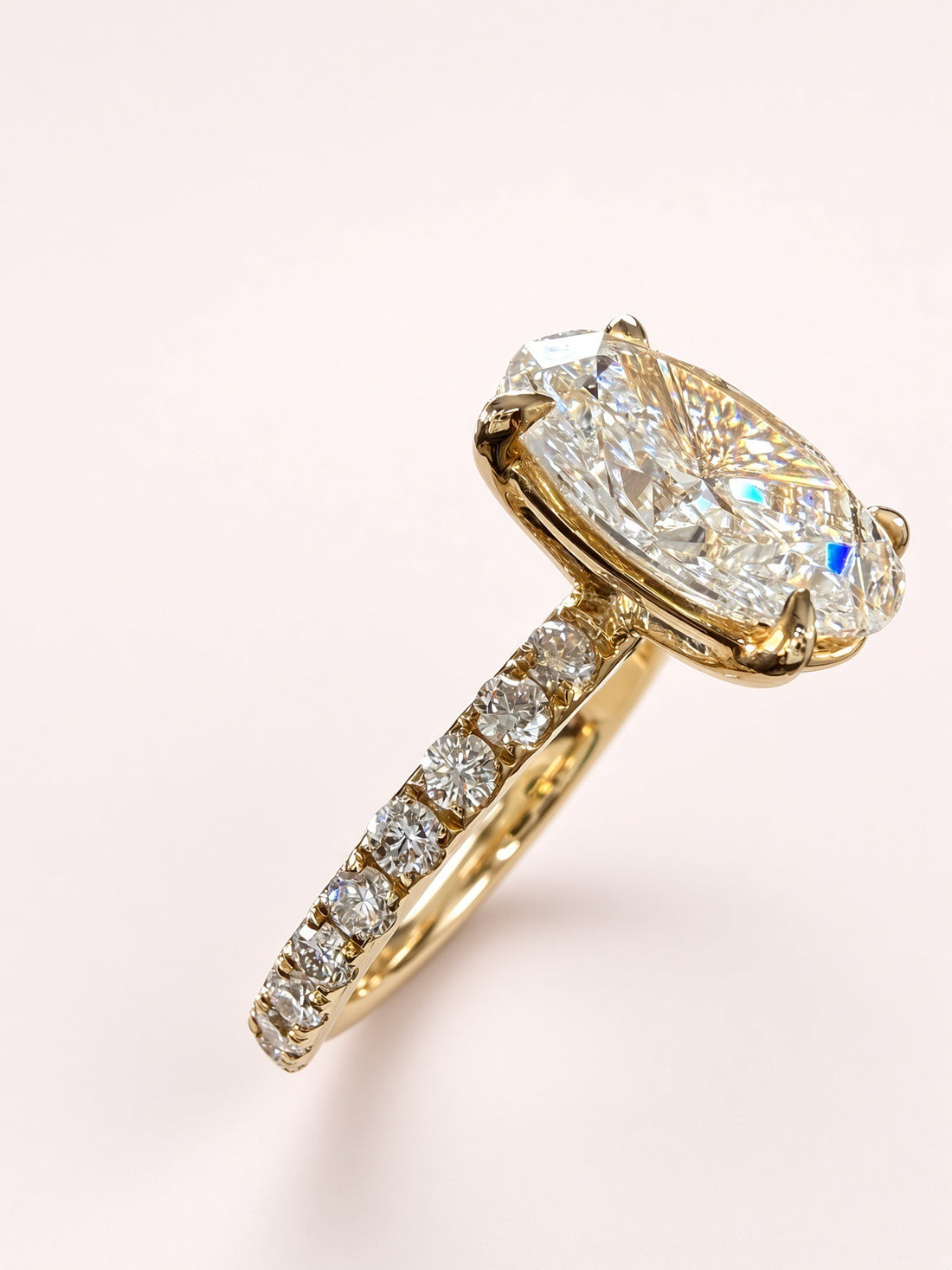 Angled close-up of an oval diamond engagement ring showing yellow-gold prongs and a diamond-set shoulder.