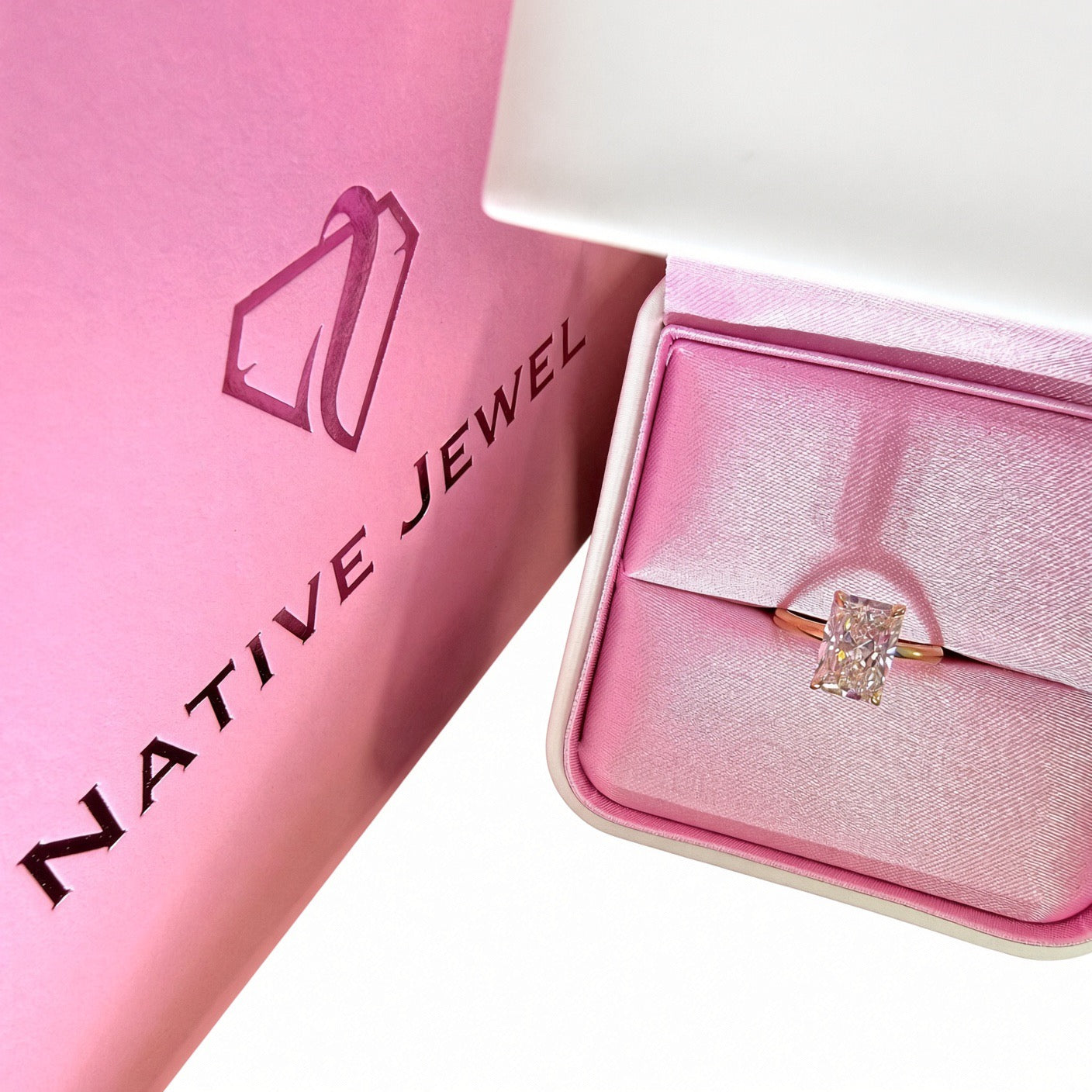 Radiant-cut diamond solitaire in a pink-lined presentation box beside a pink Native Jewel shopping bag.