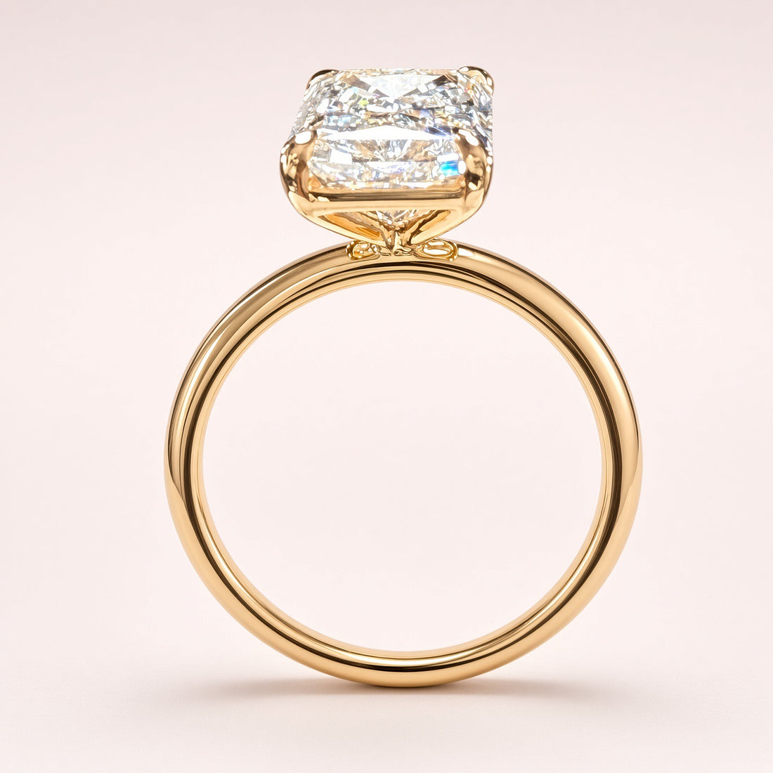Side profile of a radiant-cut diamond solitaire showing its open yellow-gold basket and polished plain band.