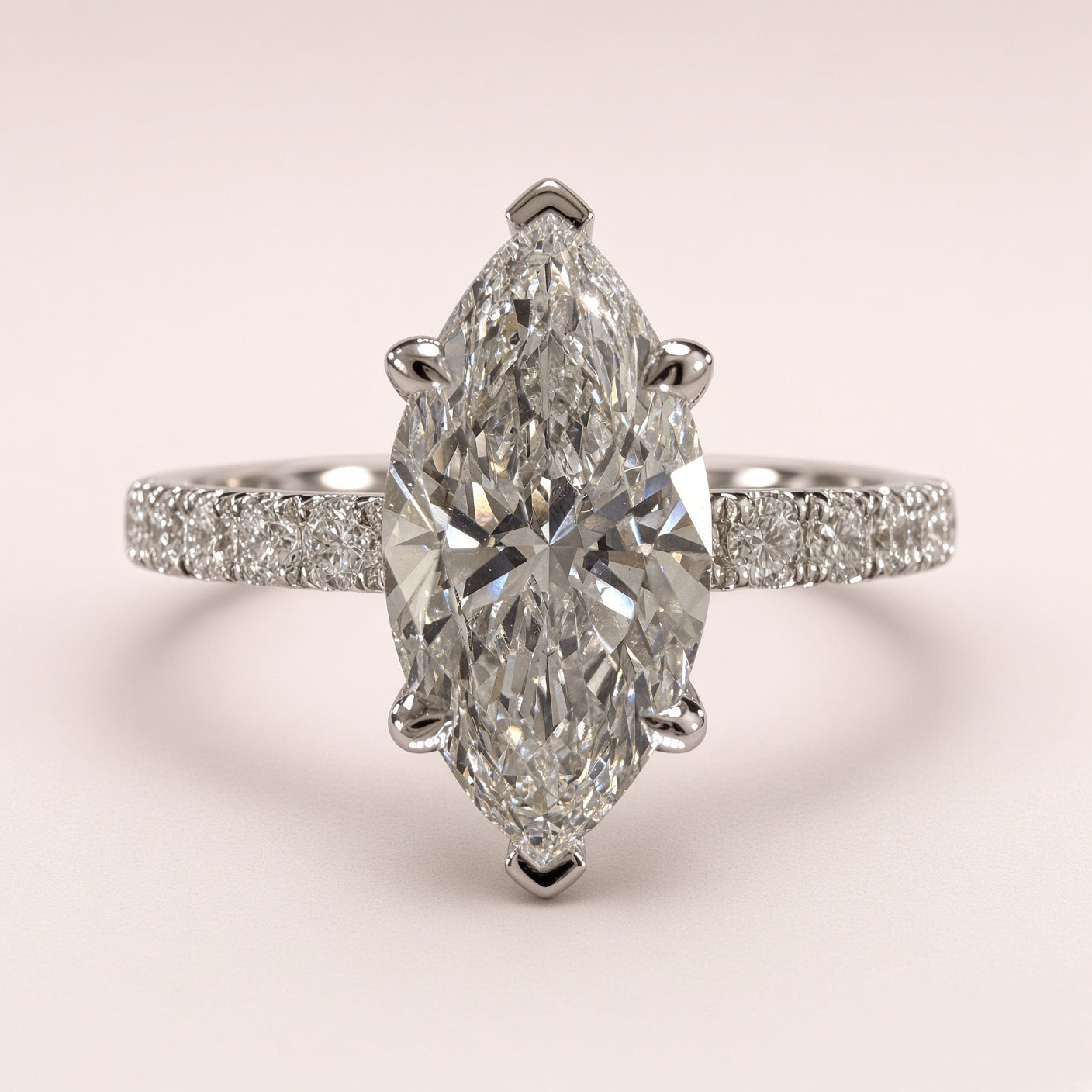 A marquise-cut diamond ring with a pavé-set band, shown on a soft light pink background.