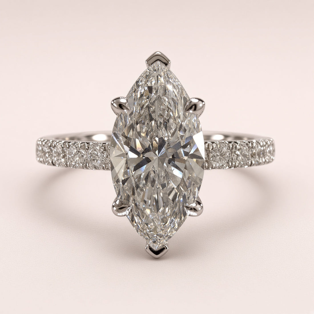 A marquise-cut diamond ring with a pavé-set band, shown on a soft light pink background.