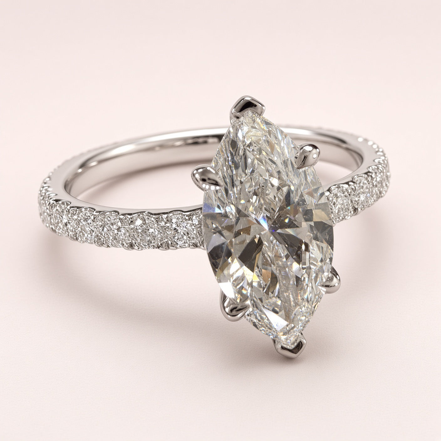 Three-quarter view of a marquise diamond pavé ring in white gold on a pale pink background.
