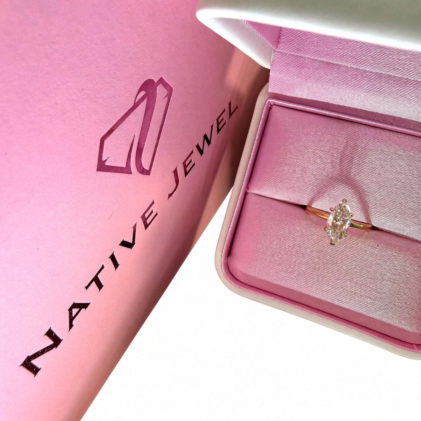 Yellow-gold marquise diamond solitaire in a pink-lined box beside a Native Jewel shopping bag on white.