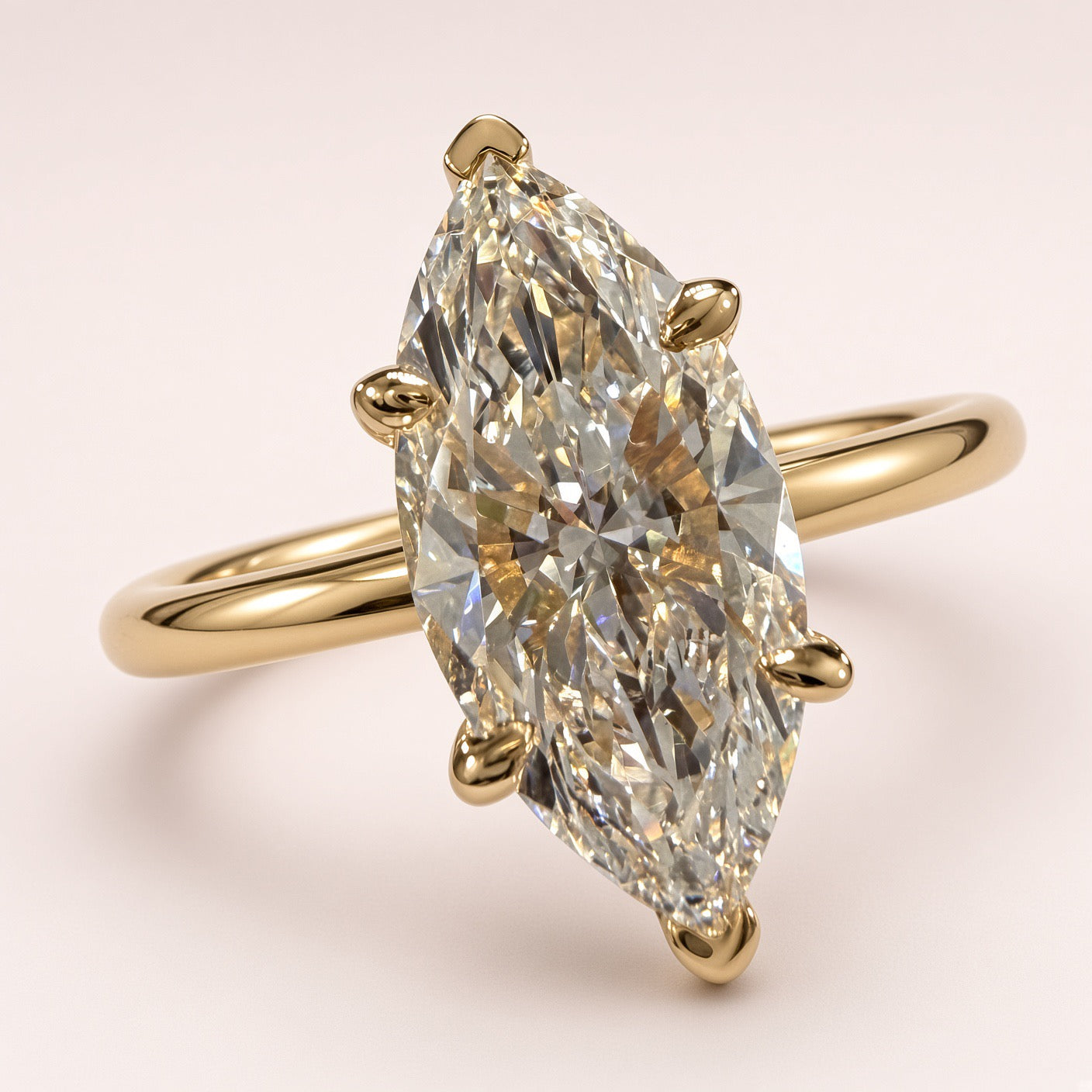 Angled front close-up of a marquise diamond solitaire showing yellow-gold tip guards and a plain band on pale pink.