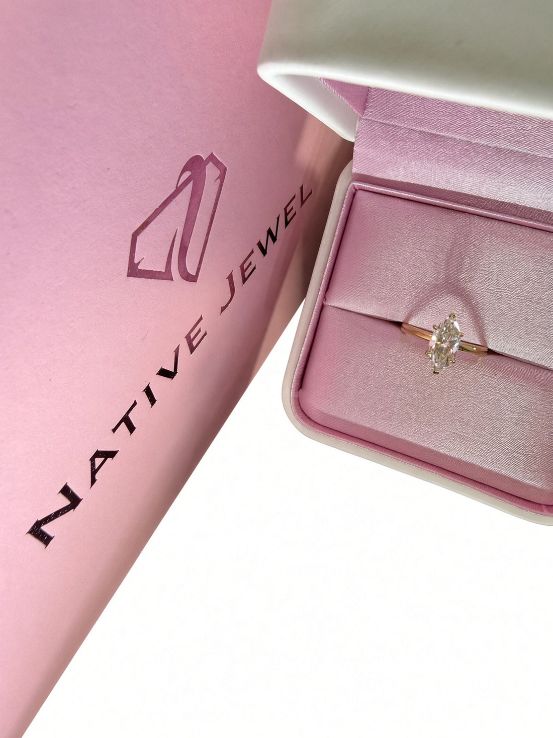 Yellow-gold marquise diamond solitaire in a pink-lined box beside a Native Jewel shopping bag on white.