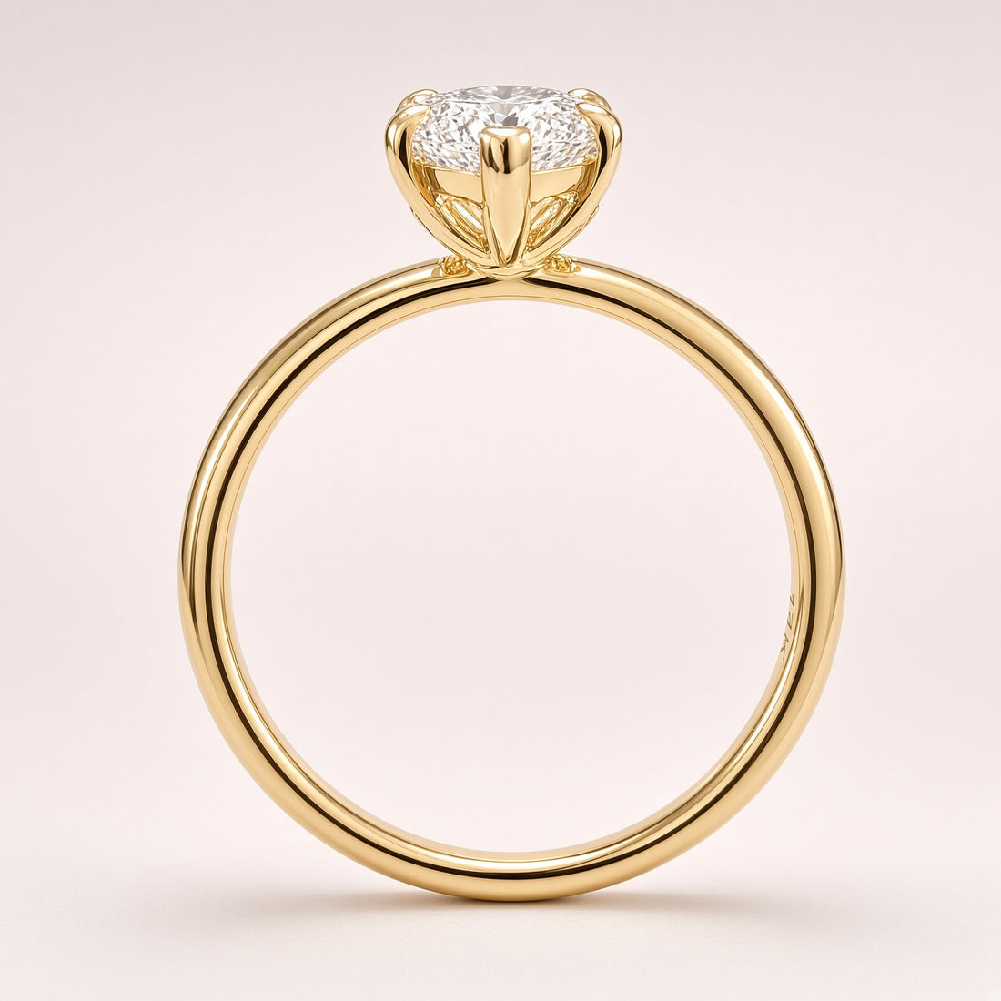 Side profile of a diamond solitaire showing an open yellow-gold basket and a plain polished band on pale pink.