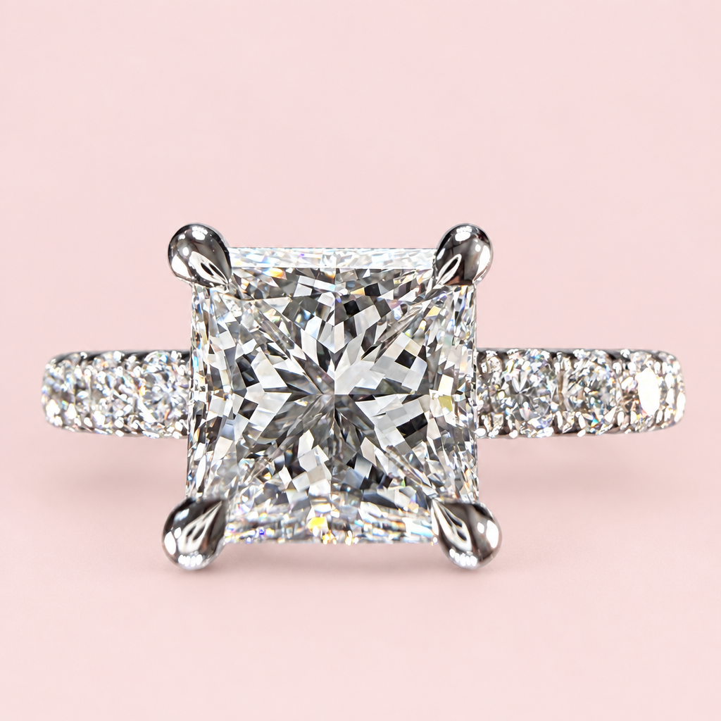 Front view of a princess-cut diamond engagement ring with four white-gold prongs and a pavé band on pink.