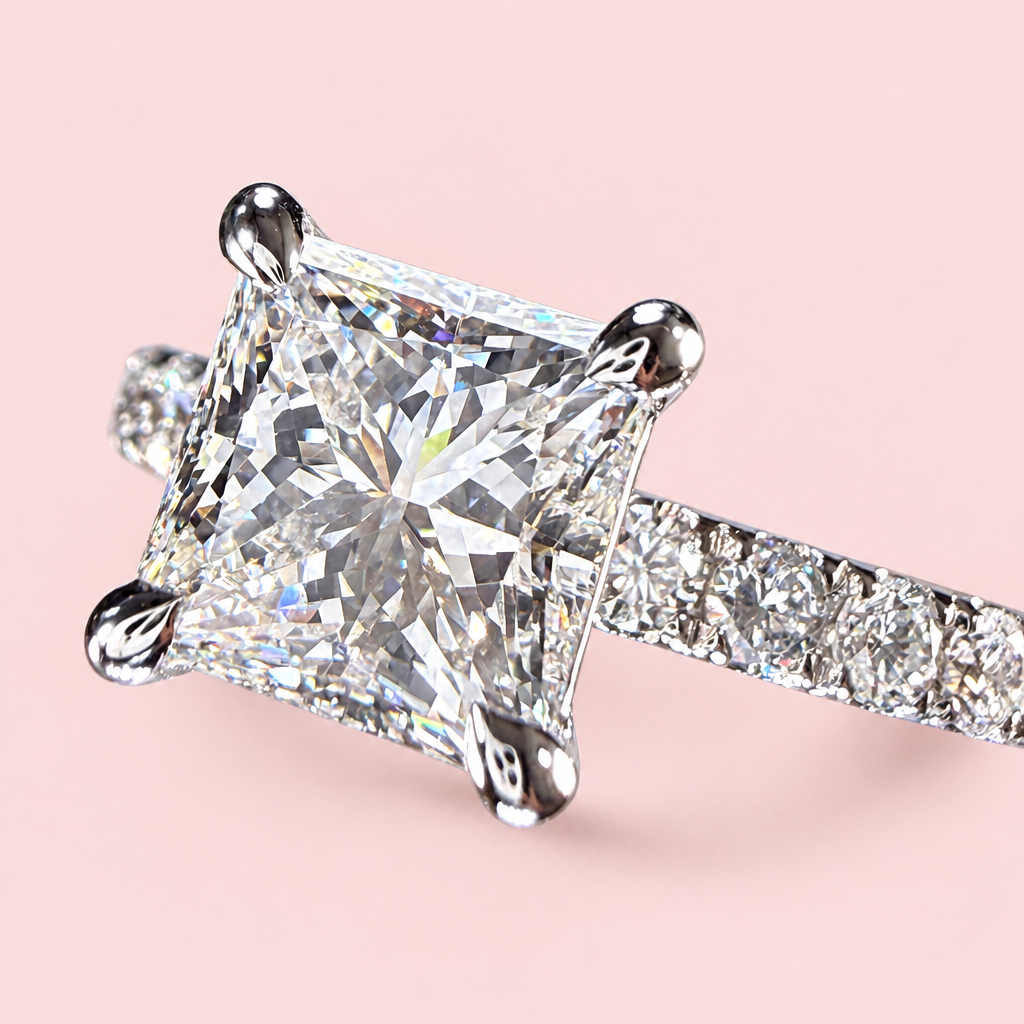 Opposite angled view of a princess-cut diamond ring showing white-gold corner prongs and a diamond-set band on pink.