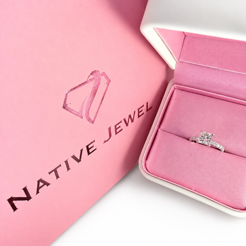 Princess-cut diamond ring in a pink-lined presentation box beside a pink Native Jewel bag on white.