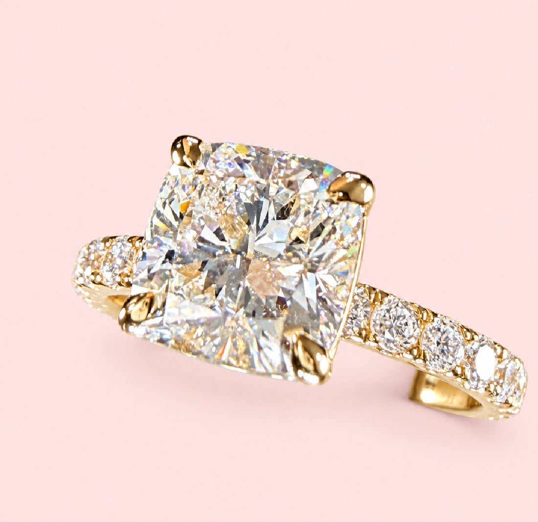 Three-quarter view of a cushion-cut diamond ring in yellow gold showing the center stone and diamond-set shoulders.