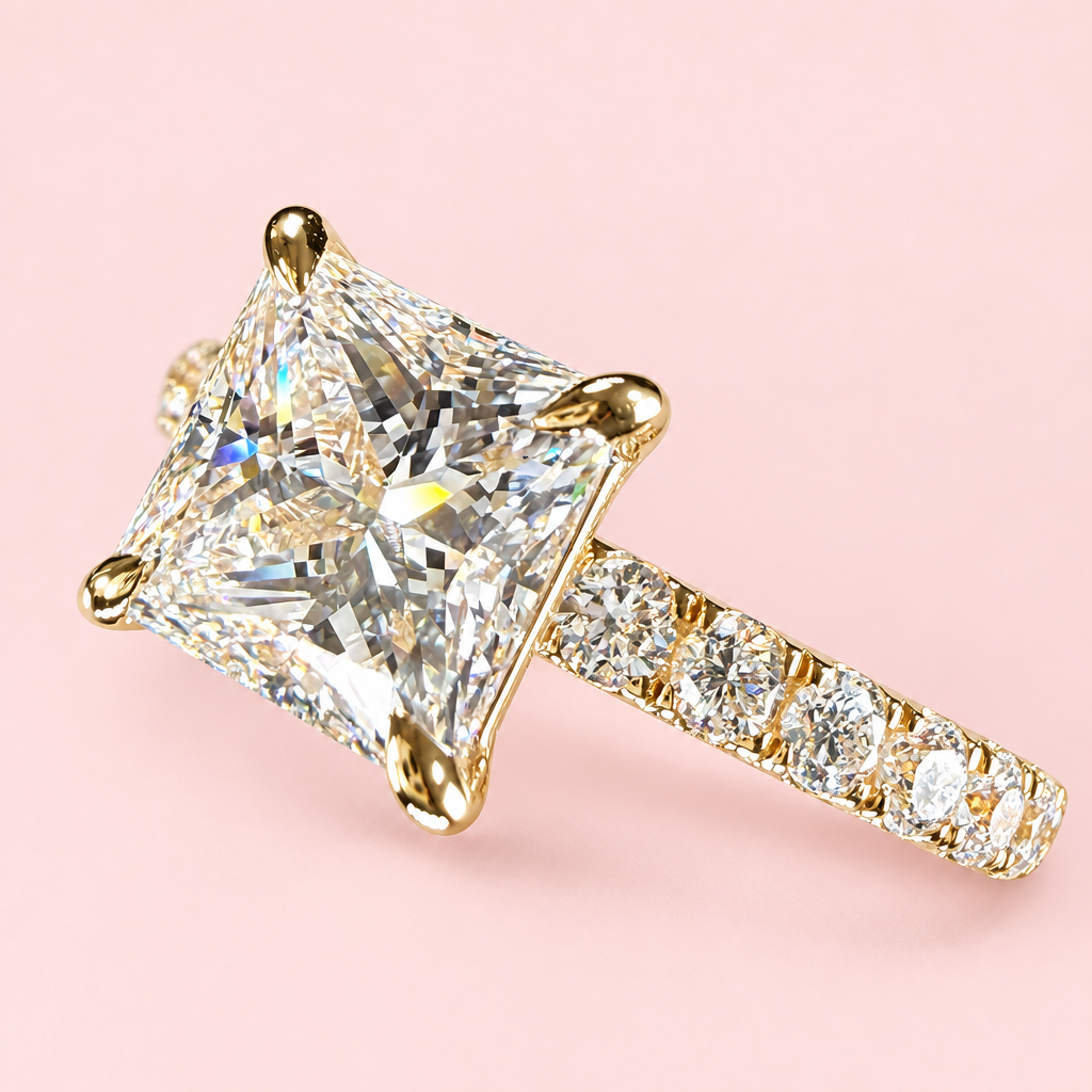Angled close-up of a princess-cut diamond ring showing yellow-gold corner prongs and a diamond-set shoulder.
