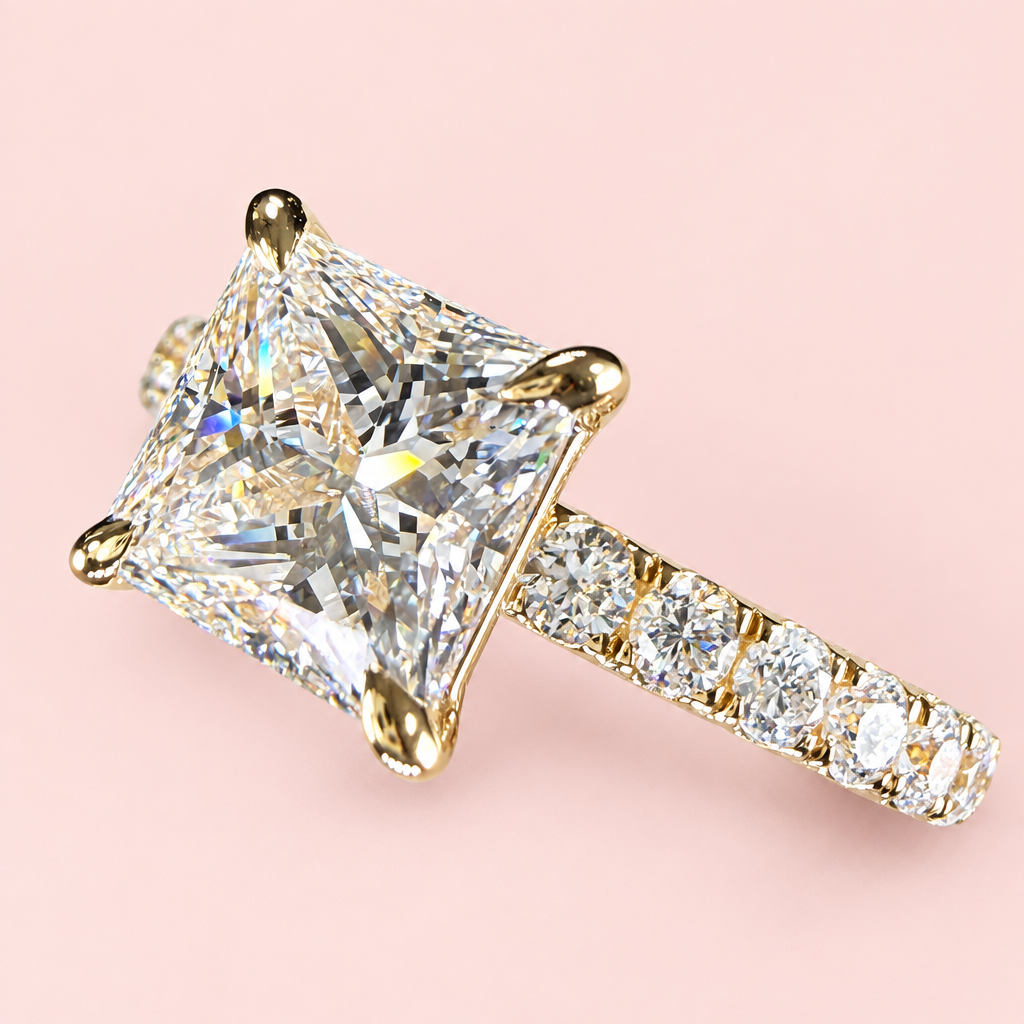 Angled close-up of a princess-cut diamond engagement ring showing yellow-gold corner prongs and a pavé shoulder.