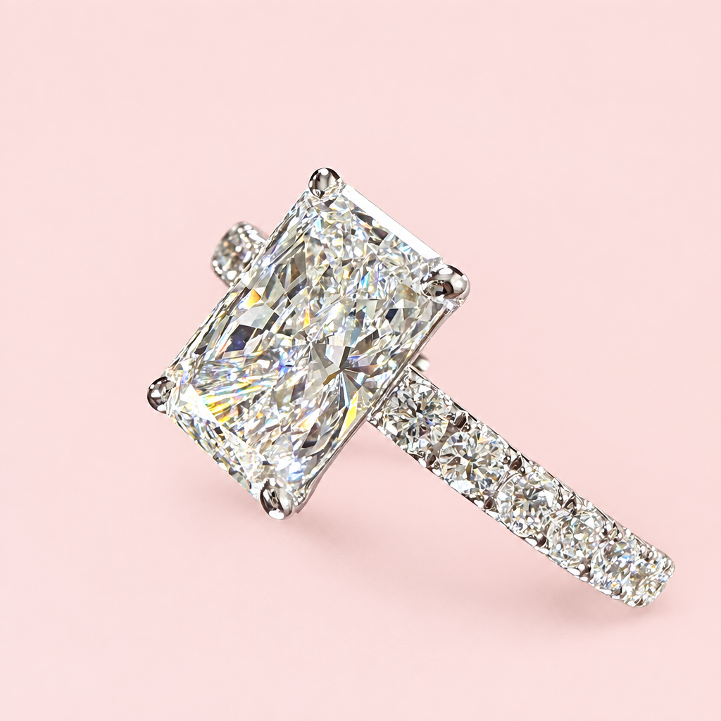 Angled close-up of a radiant-cut diamond ring showing four white-gold prongs and a diamond-set shoulder.