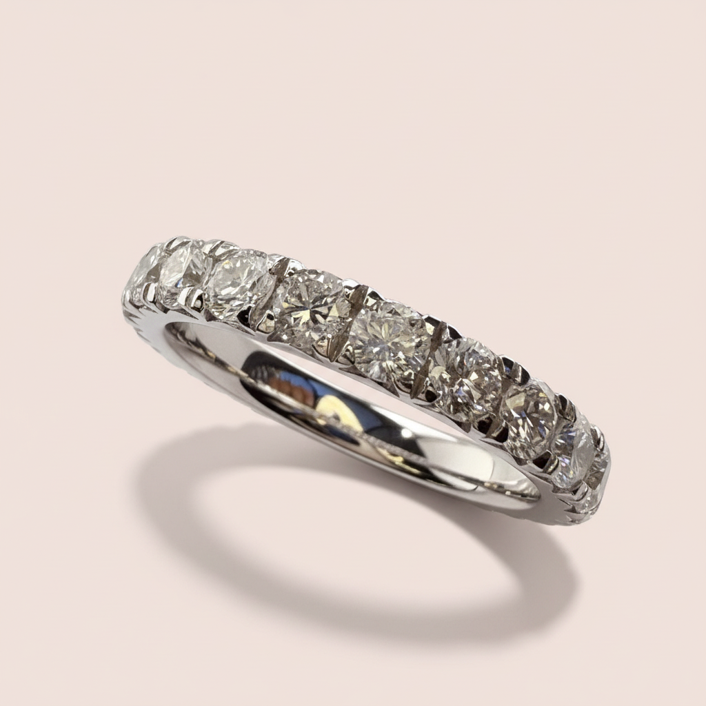 Angled view of a white-gold wedding band showing round diamonds and a polished inner band on pale pink.