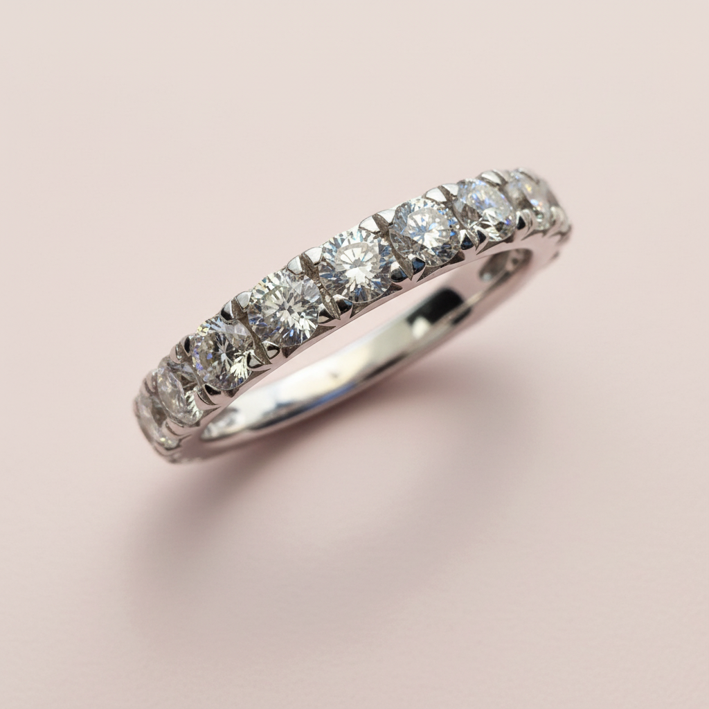 Close front angle of a white-gold wedding band showing round diamonds and shared prongs on pale pink.
