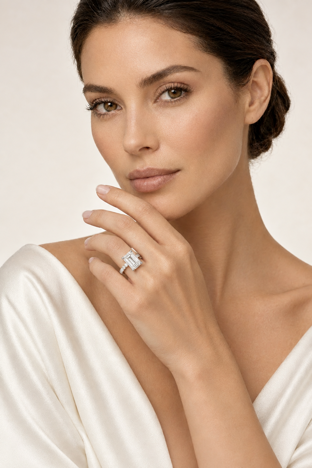 Model wearing an emerald-cut diamond engagement ring with a white-gold diamond-set band near her face.