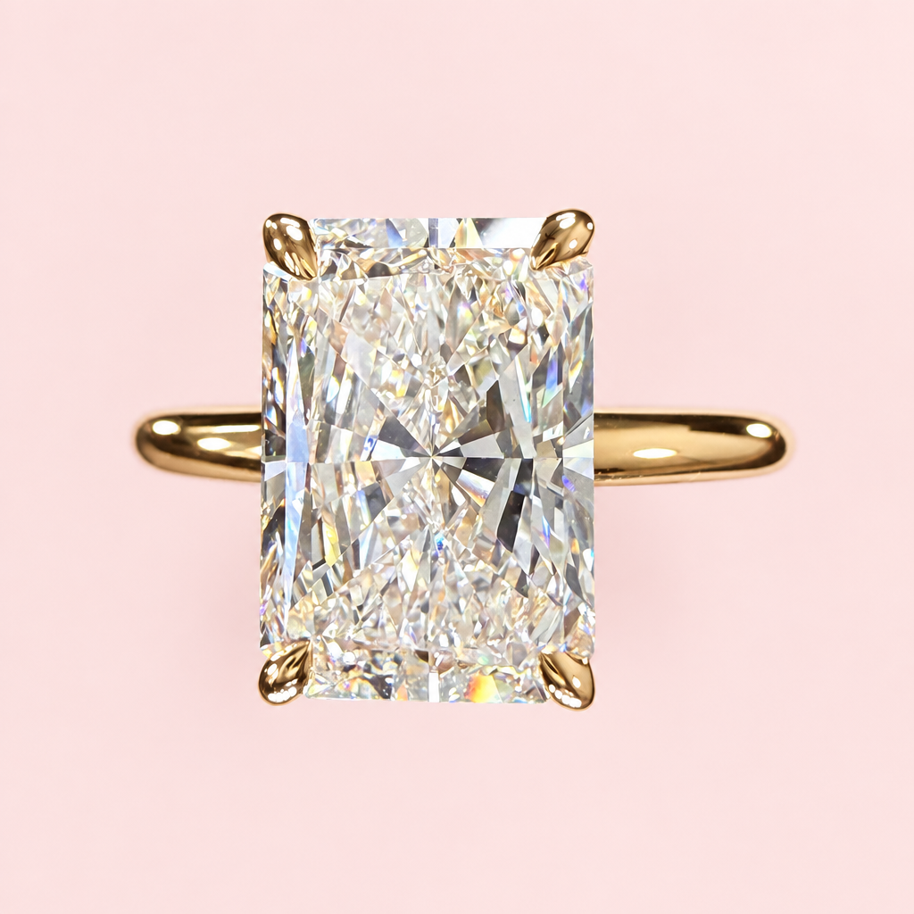 Front view of a radiant-cut diamond solitaire with four yellow-gold prongs and a plain band on pink.