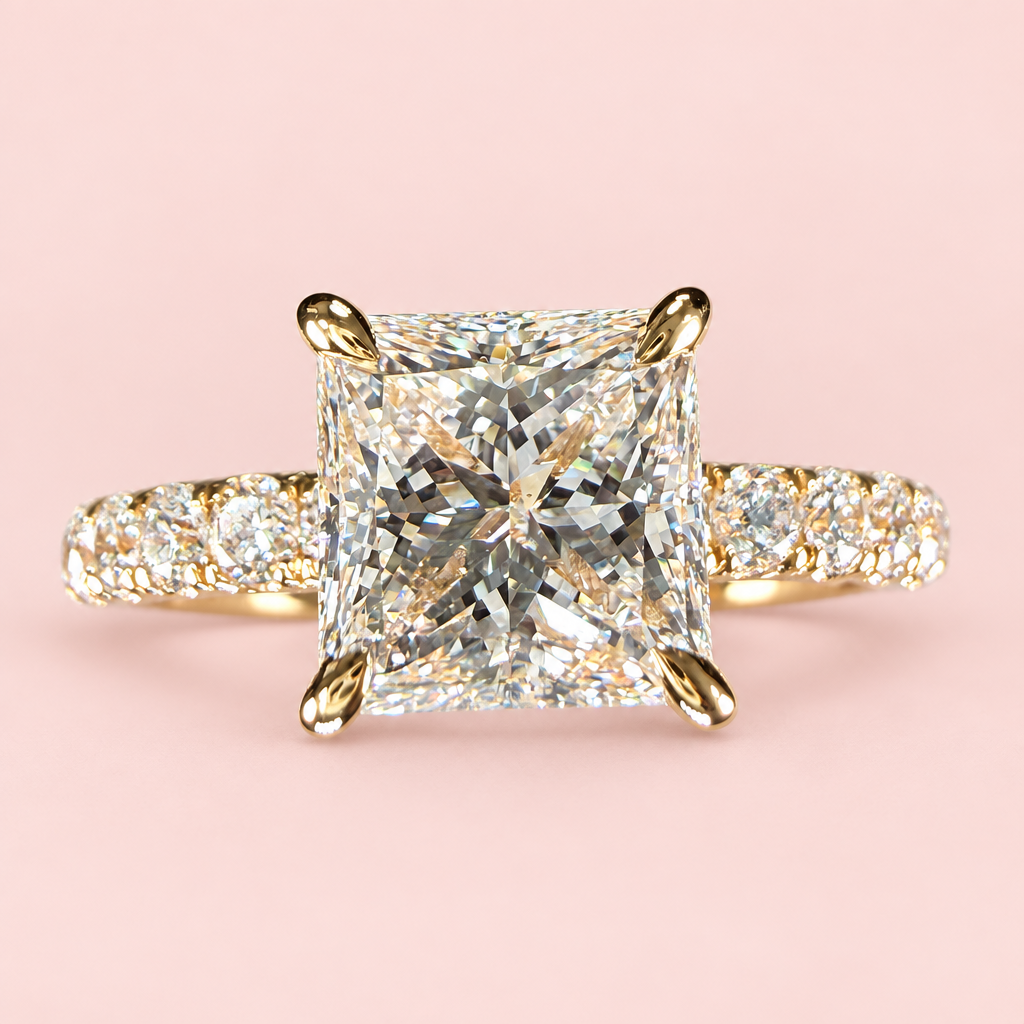 Front view of a princess-cut diamond engagement ring with four yellow-gold prongs and a pavé band on pink.