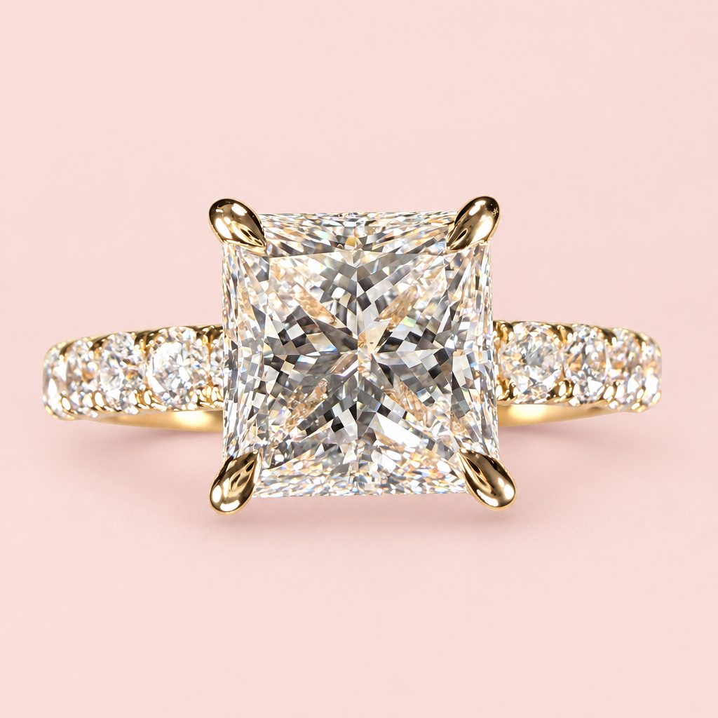Front close-up of a princess-cut diamond engagement ring with yellow-gold corner prongs and a diamond-set band.
