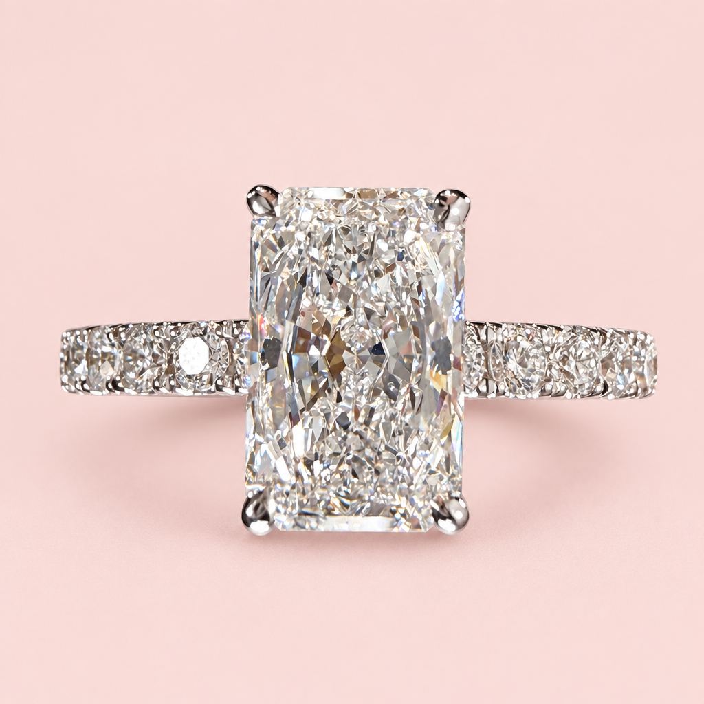 Front view of a radiant-cut diamond engagement ring with four white-gold prongs and a pavé band on pink.