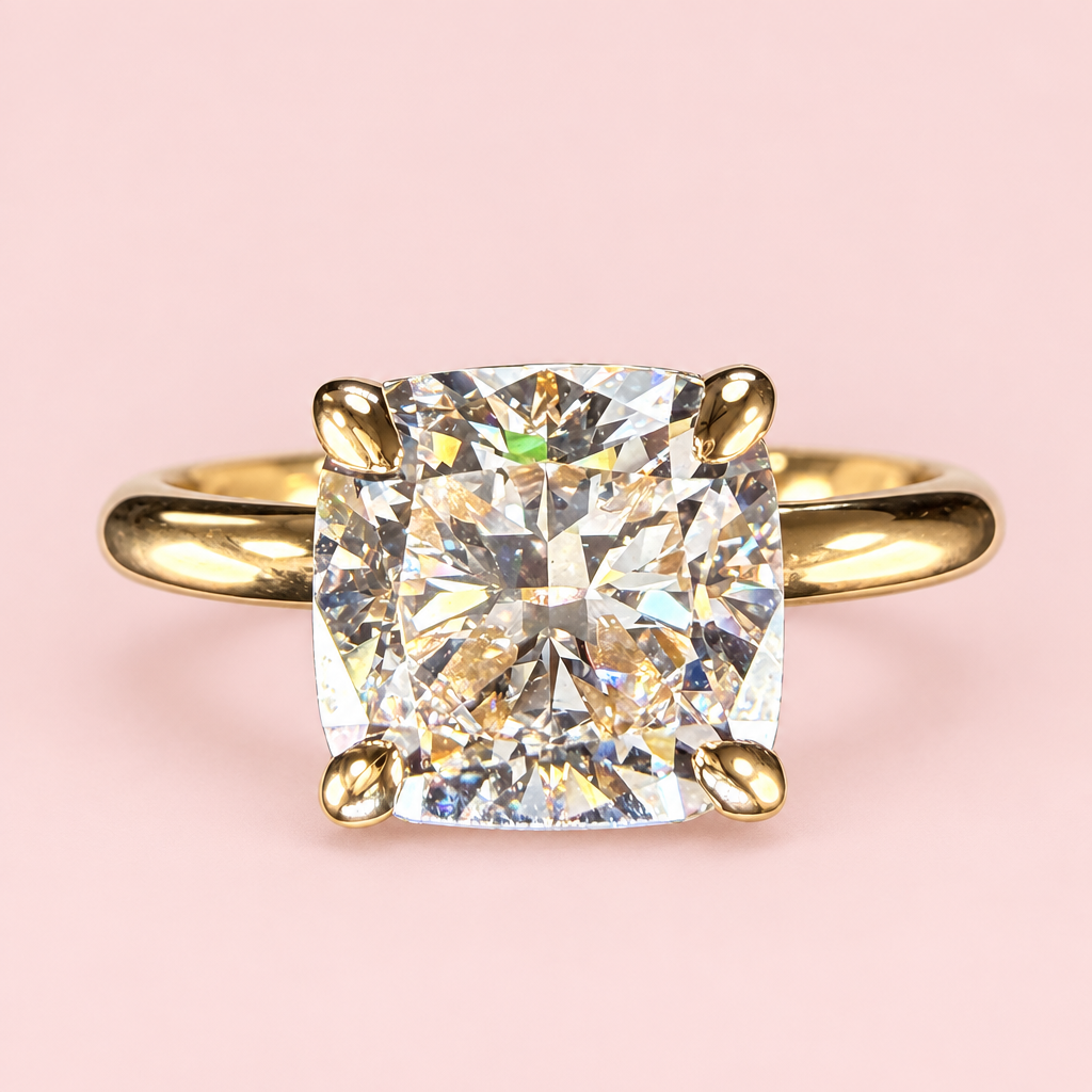 Front view of a cushion-cut diamond solitaire with four yellow-gold prongs and a polished plain band on pink.