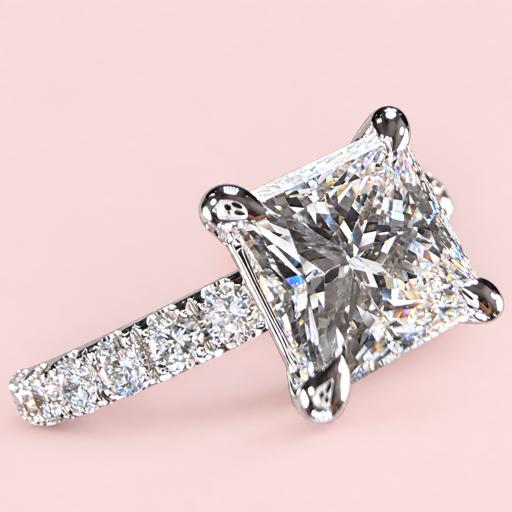 Angled front view of a princess-cut diamond engagement ring with white-gold corner prongs and a pavé band.