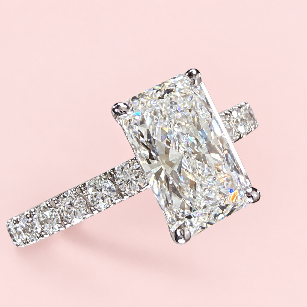 Opposite angled view of a radiant-cut diamond engagement ring showing white-gold prongs and a pavé shoulder.