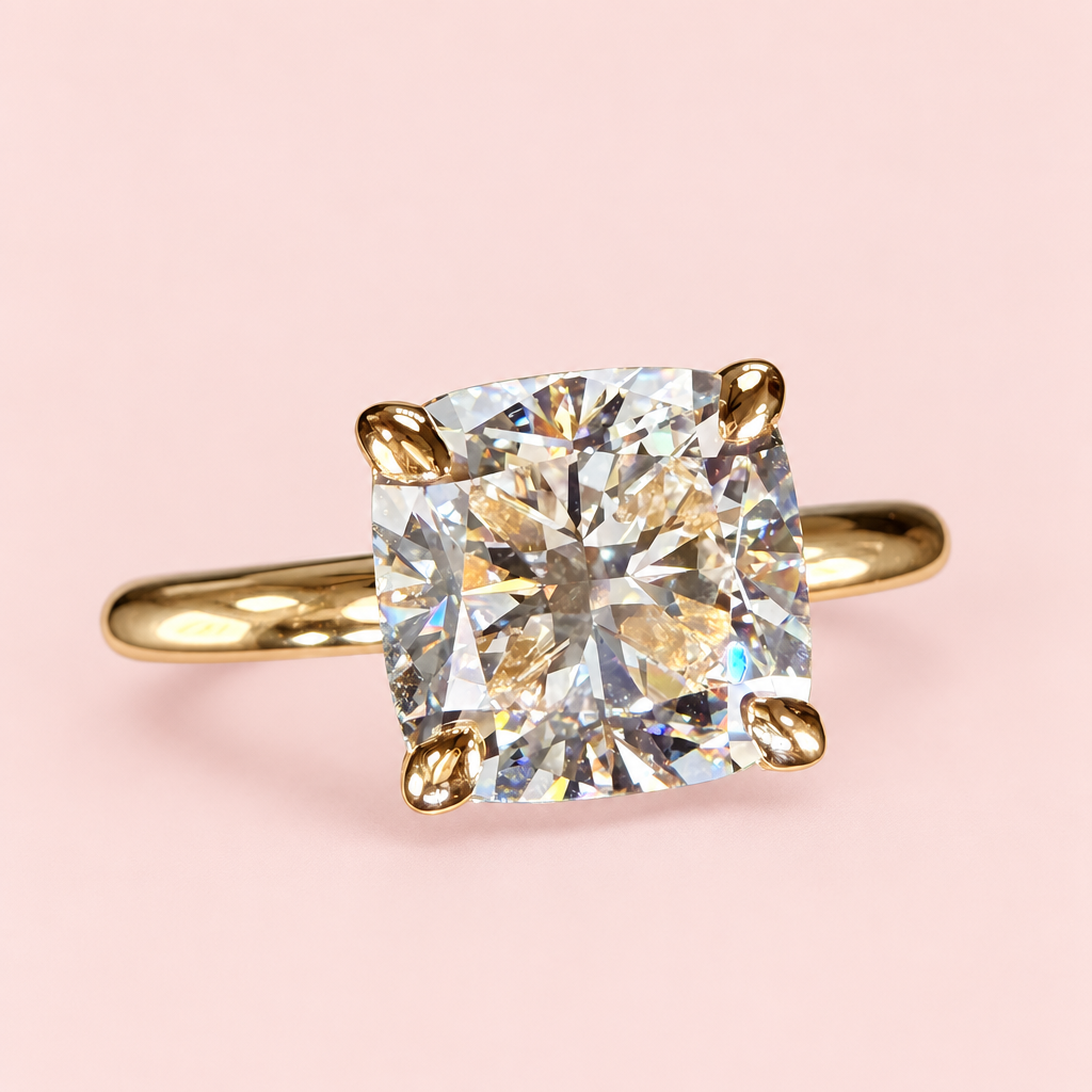 Opposite front angle of a cushion-cut diamond solitaire with four yellow-gold prongs and a plain band on pink.