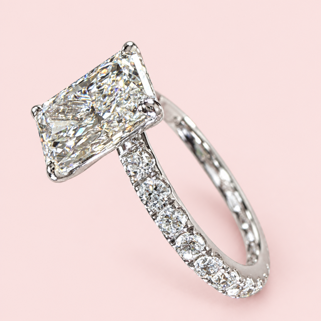 Side angle of a radiant-cut diamond engagement ring showing a raised white-gold setting and diamond-set band.